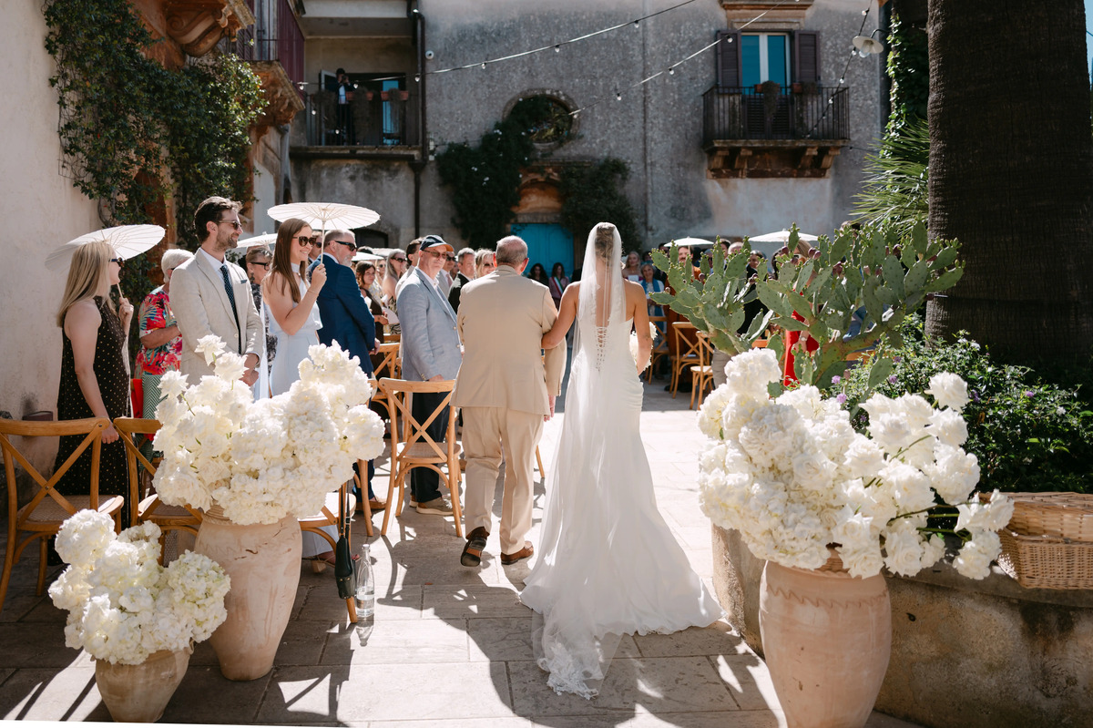 Bride walking to ceremony with her father at an elegant Italian courtyard wedding