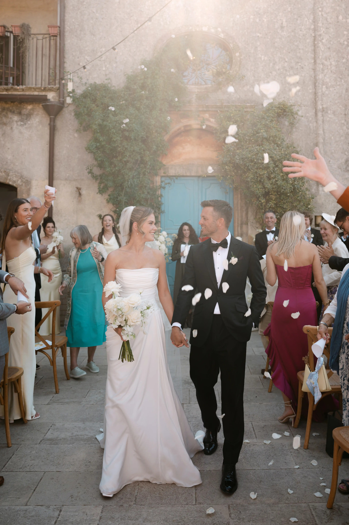 Newlywed couple walking through flower petals after their outdoor wedding ceremony in Sicily.