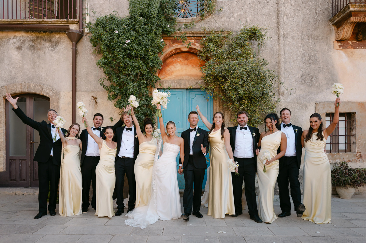 Bride and groom celebrating with bridesmaids and groomsmen in front of a rustic Italian villa.