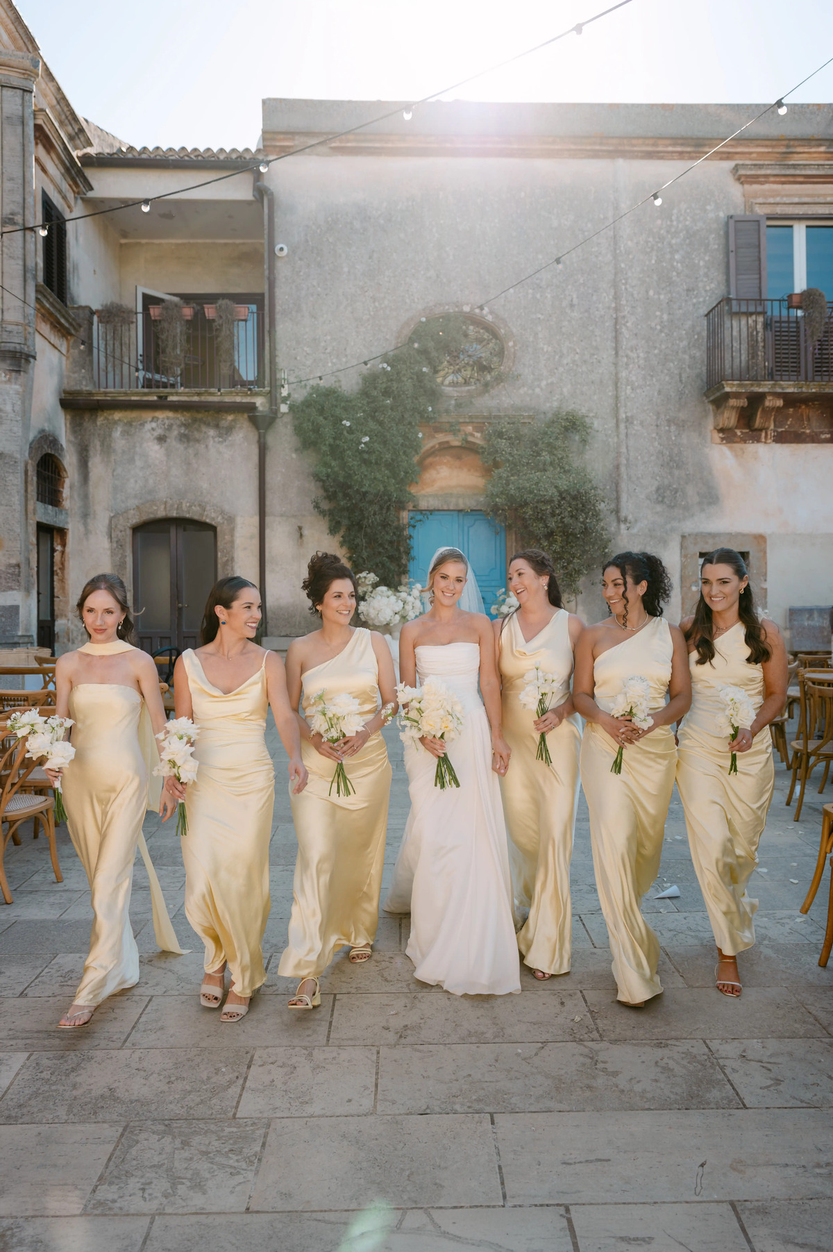 Bride walking with bridesmaids in champagne satin dresses at a luxury Sicilian wedding venue.