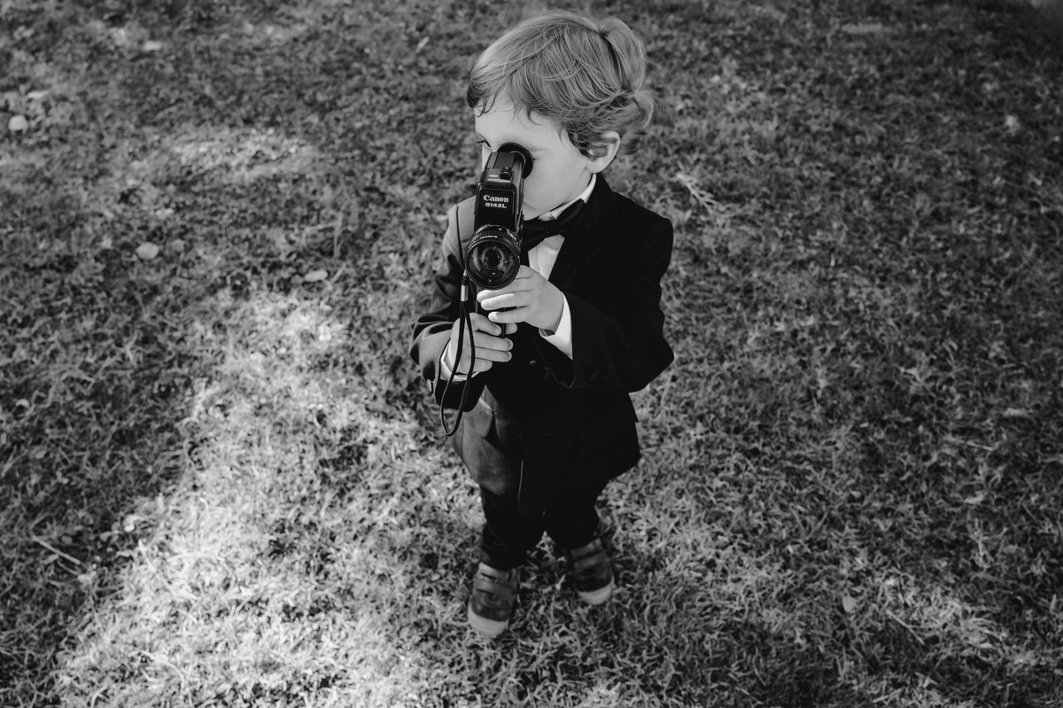 Little boy dressed in a tuxedo holding a vintage video camera during an Italian wedding celebration.