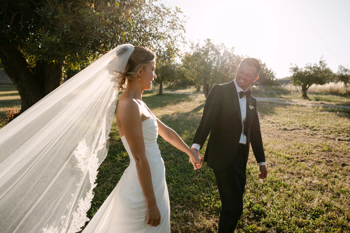 Bride and groom holding hands while walking through golden sunset light at a countryside wedding in Italy.