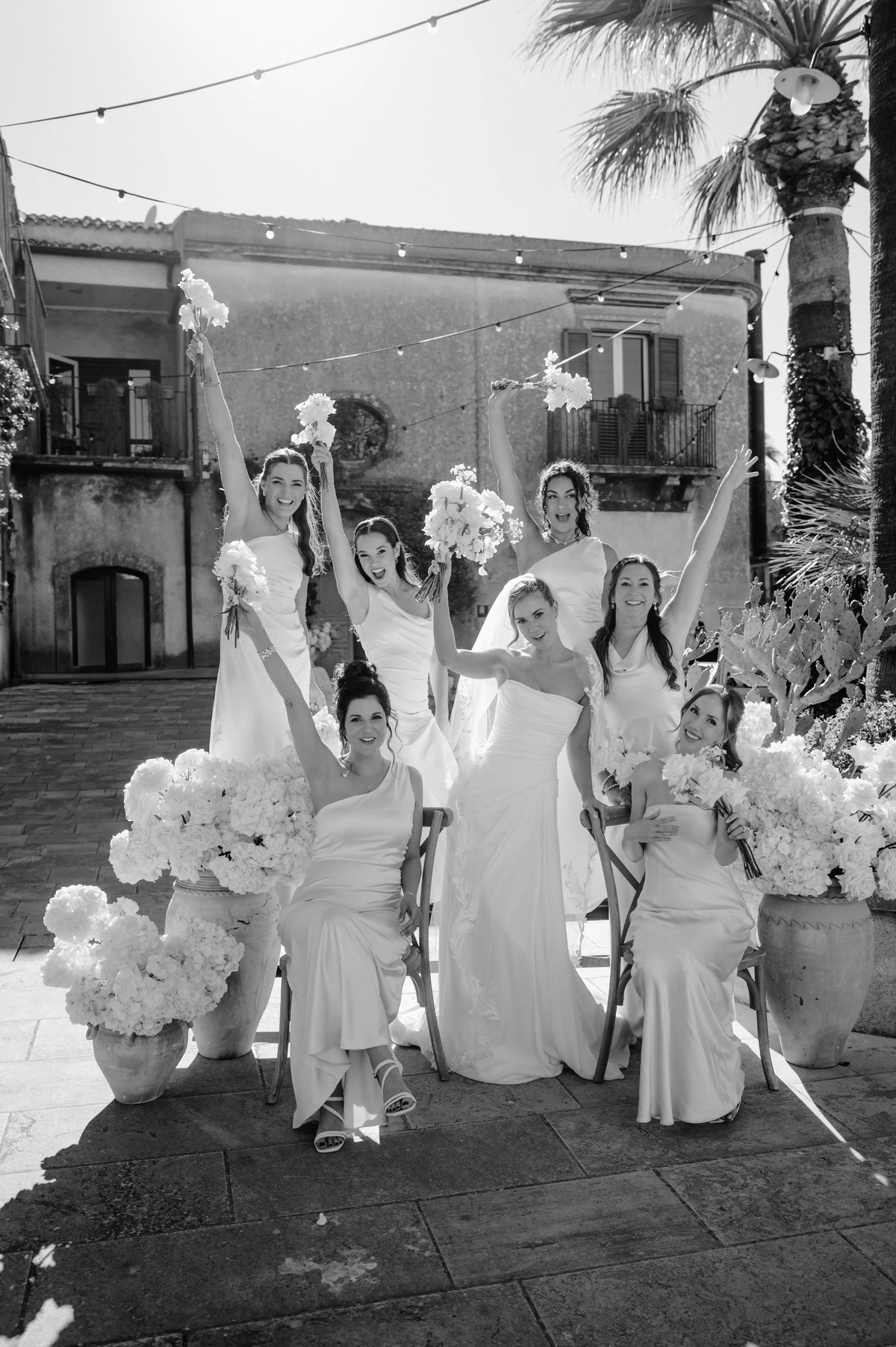 Black and white bridal party portrait with bridesmaids celebrating in a historic Sicilian courtyard.