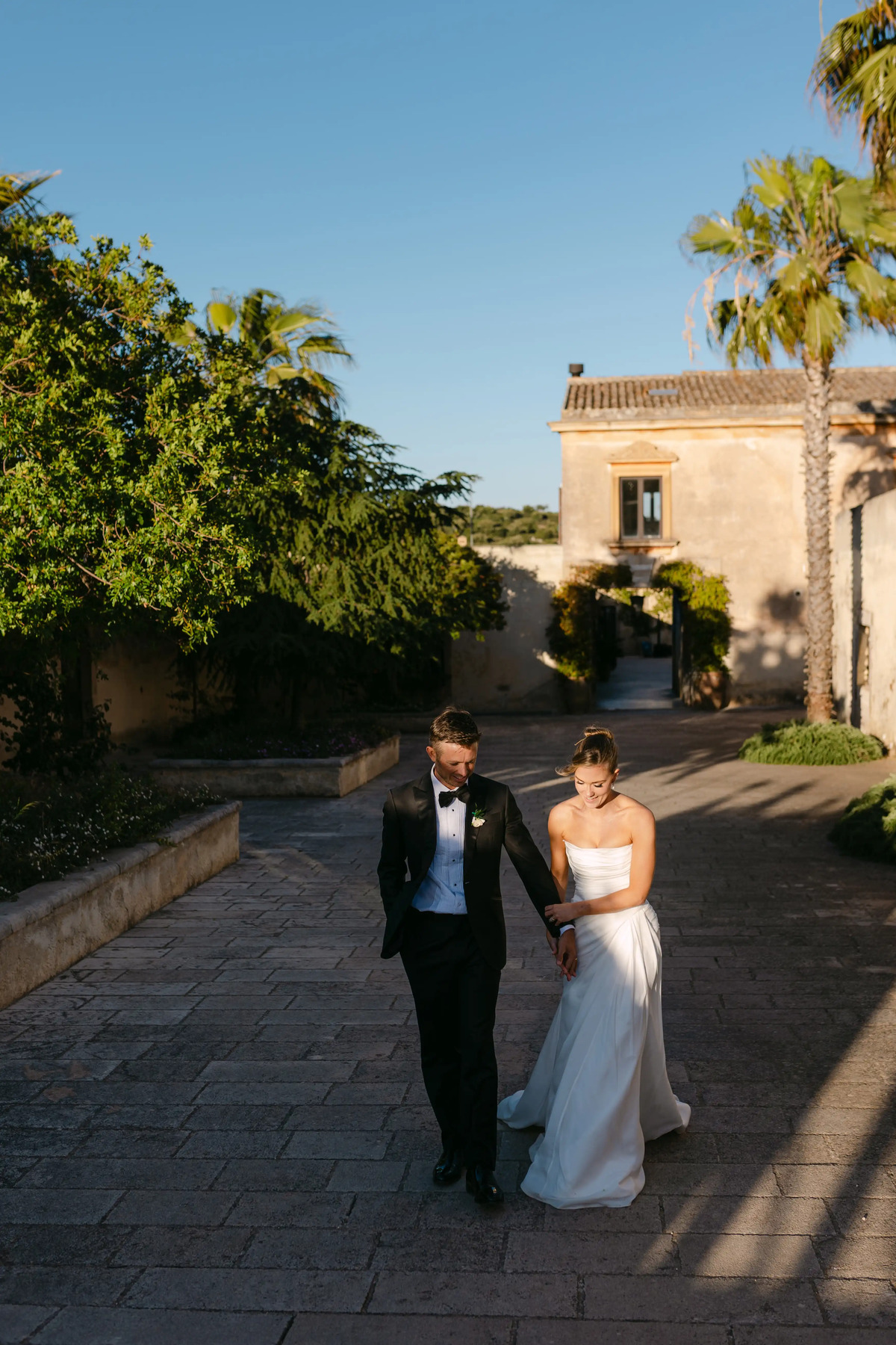 Bride and groom walking together through a historic Italian villa courtyard at golden hour.