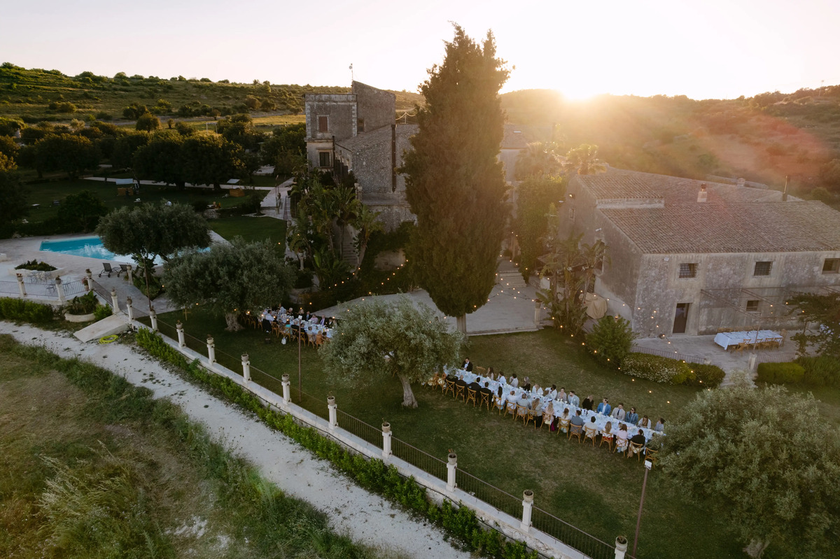 Aerial drone view of a luxury wedding reception at a historic countryside villa in Sicily at sunset.