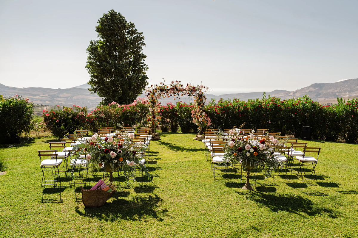Outdoor elopement ceremony setup in the Sicilian countryside with floral arch and panoramic views.